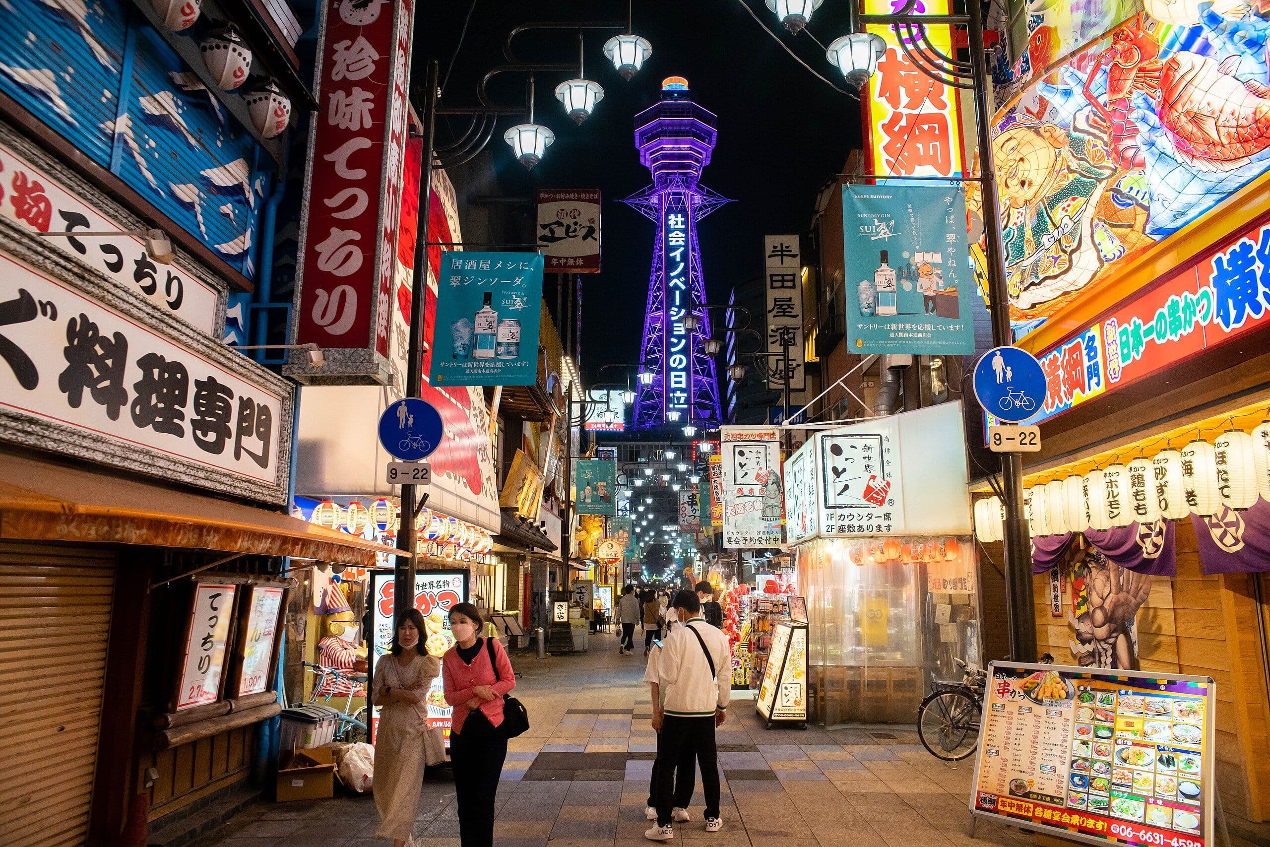 Osaka's Shinsekai at night, with Tsutenkaku Tower glowing above bustling streets.
